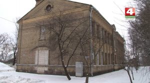 Старое кирпичное здание зимой олицетворяет исторический облик Гродно, окруженное голыми деревьями и снегом, с логотипом телевидения в углу.