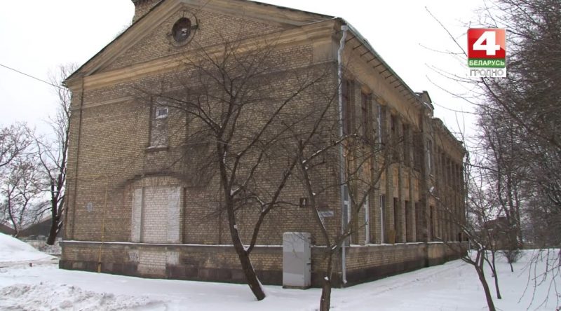 Старое кирпичное здание зимой олицетворяет исторический облик Гродно, окруженное голыми деревьями и снегом, с логотипом телевидения в углу.